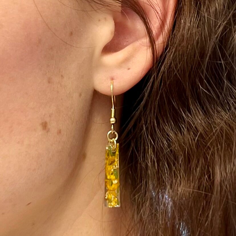 A close up of a women wearing sunflower resin bar earrings which are attached to gold French wires.